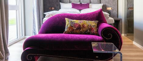 A modern bedroom with a large bed, a purple sofa, and a clear glass coffee table.
