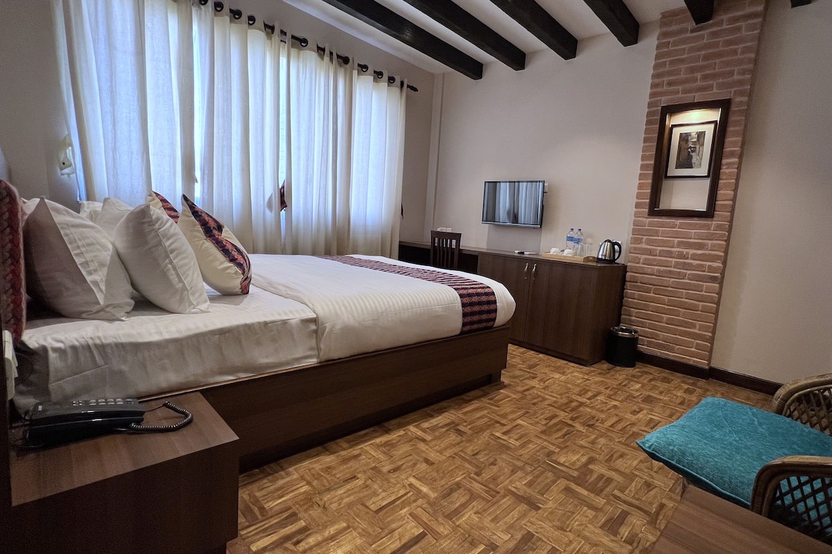 A hotel room with a bed, a desk with a telephone, a chair, a television, and a brick wall.