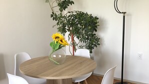 A dining area with a round wooden table, white chairs, a purple rug, and a potted plant with a sunflower.