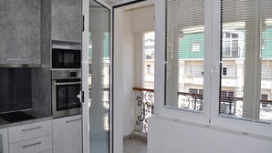 A modern kitchen with a built-in oven and microwave, a balcony with metal railings, and a view of neighboring buildings.