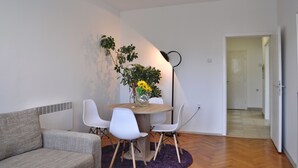 A modern living room with a sofa, a dining table with chairs, a potted plant, and a ceiling light fixture.