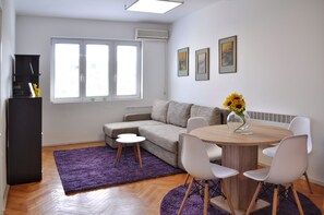 Una sala moderna con un sofá, una mesa de comedor con sillas, un tapete morado y un jarrón con girasoles.