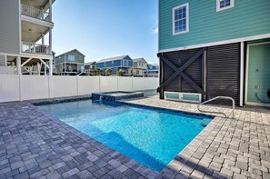 Une piscine bordée de briques, une terrasse en bois et, en arrière-plan, une vue sur des immeubles à plusieurs étages.