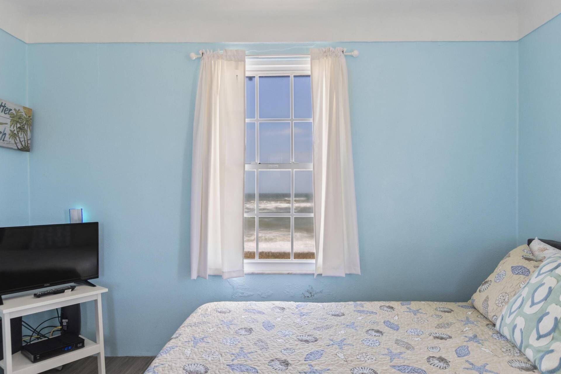 Une chambre à coucher avec un lit, un téléviseur posé sur un meuble et une fenêtre avec des rideaux.