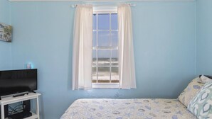 Une chambre à coucher avec un lit, un téléviseur posé sur un meuble et une fenêtre avec des rideaux.