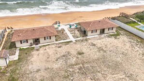 Une propriété située en bord de mer, comprenant deux maisons de plain-pied, une plage de sable et une vue sur l’océan.