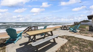 Un espace aménagé près de la plage, avec des tables de pique-nique en bois et des fauteuils Adirondack, offrant une vue sur l’océan.