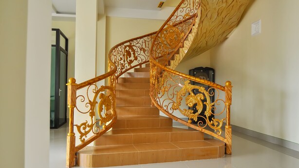 A spiral staircase with ornate golden railings and wooden steps. - OYO 838 Sanjaya Homestay Syariah (Bukittinggi)