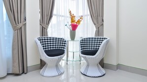 A room with two white wicker chairs with black cushions, a glass table with a pink vase of flowers, and beige curtains. - OYO 838 Sanjaya Homestay Syariah (Bukittinggi)