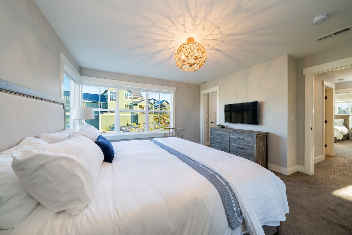 Ein Schlafzimmer mit einem großen Bett, einem Fernseher und Blick auf ein Haus durch ein Fenster.