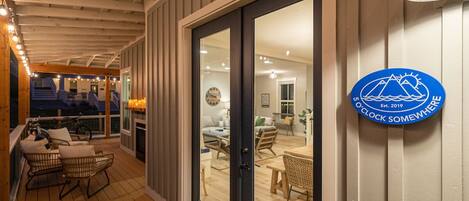 A wooden deck with outdoor seating and a view into a well-lit interior space.