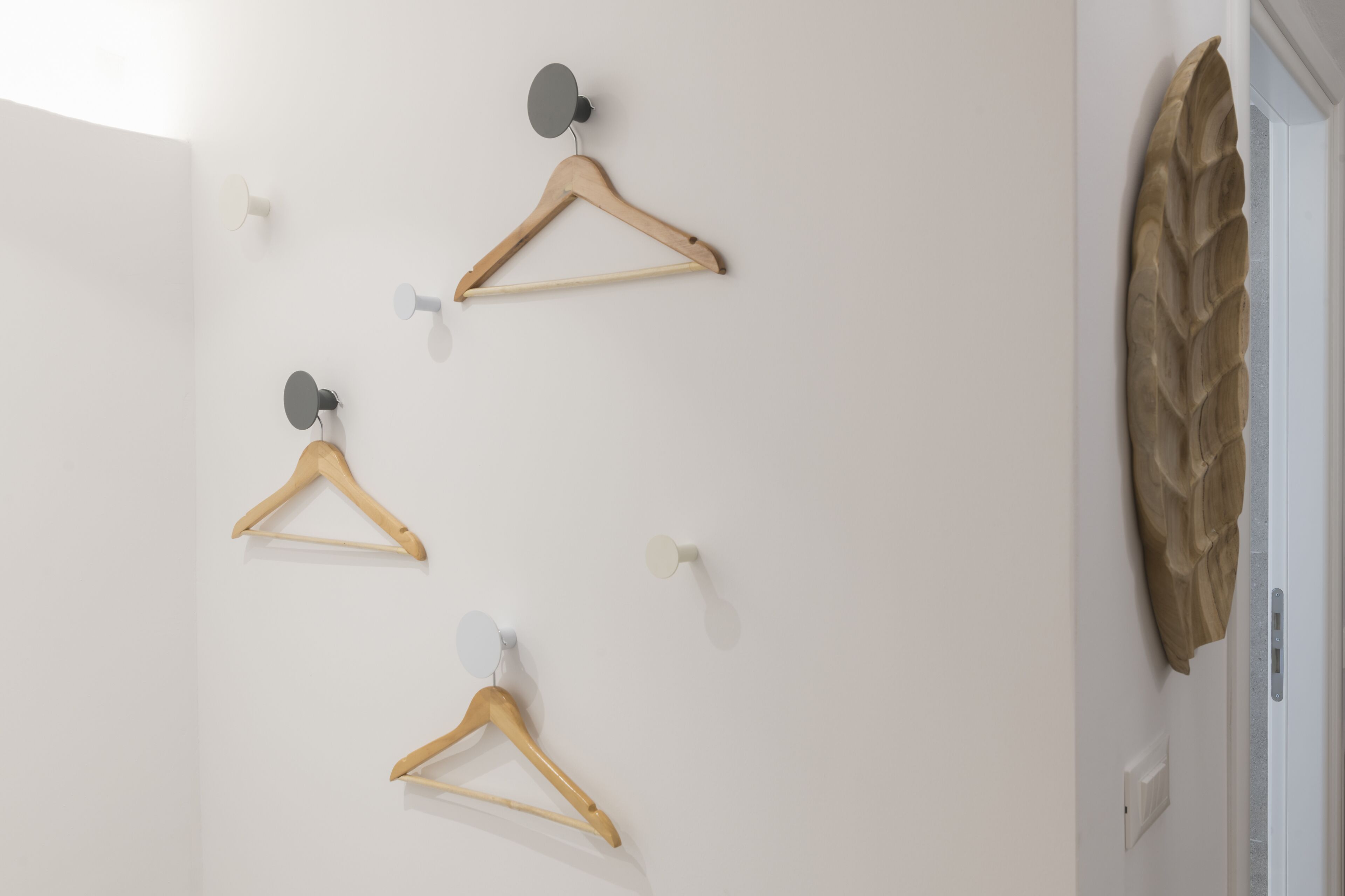 A wall with three wooden hangers and a decorative leaf-like object.