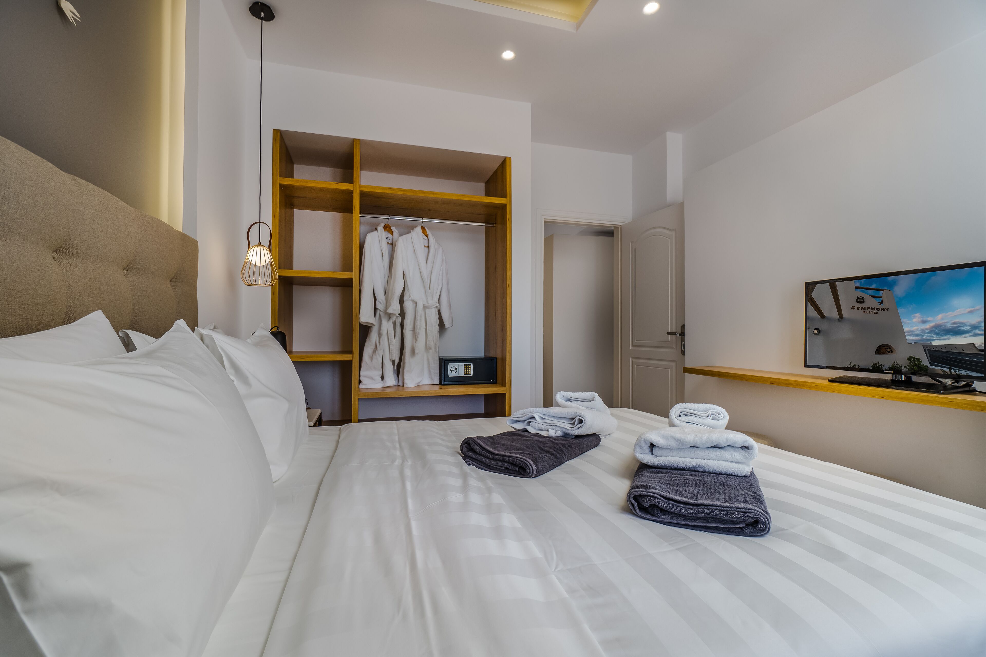 A neatly made bed with towels, a wooden wardrobe, and a television on a stand.