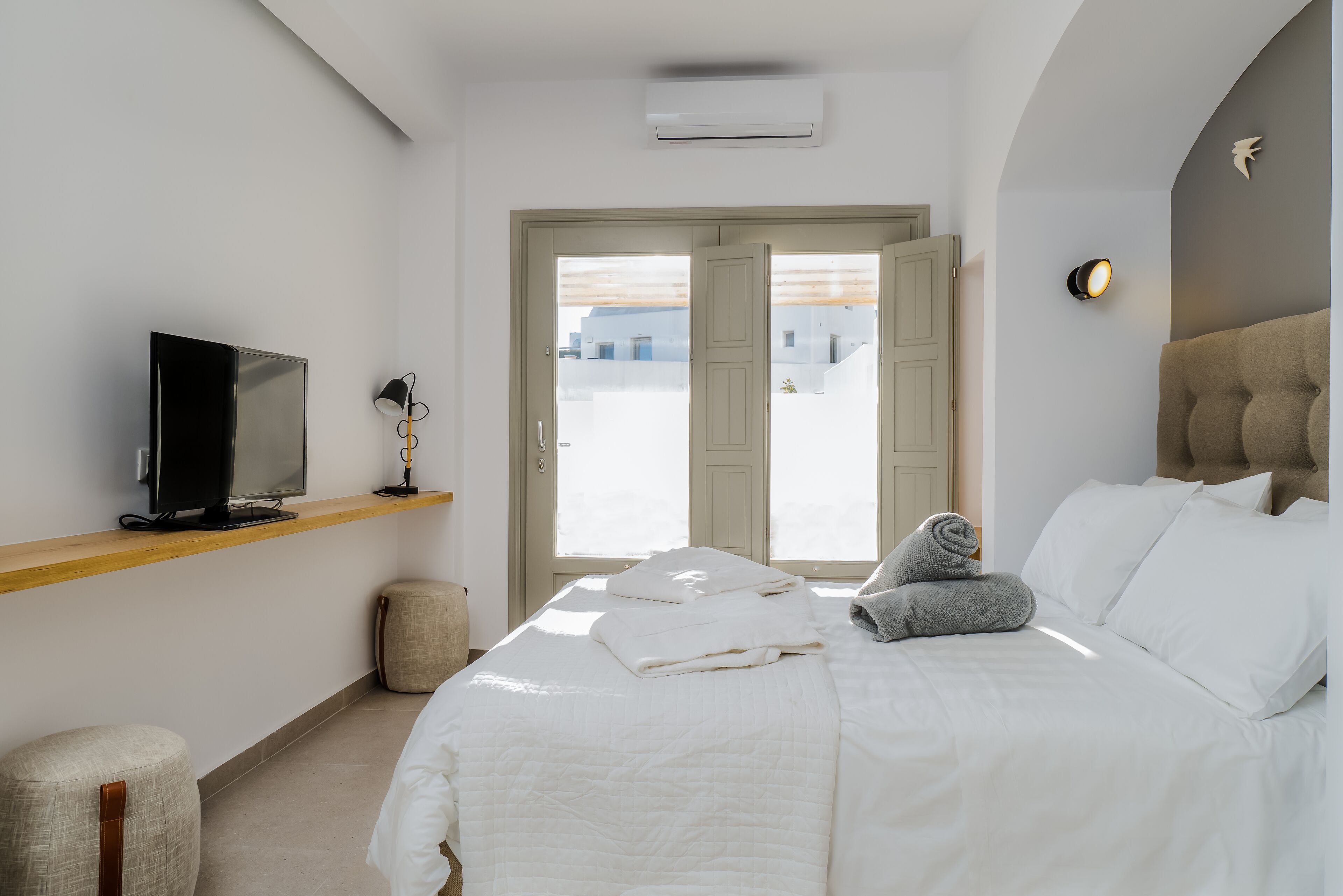 A modern hotel room with a bed, a TV, a small table, and a door leading to a balcony.