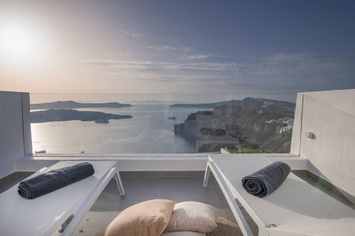 A balcony with two sun loungers, a view of a coastal landscape, and a clear sky.