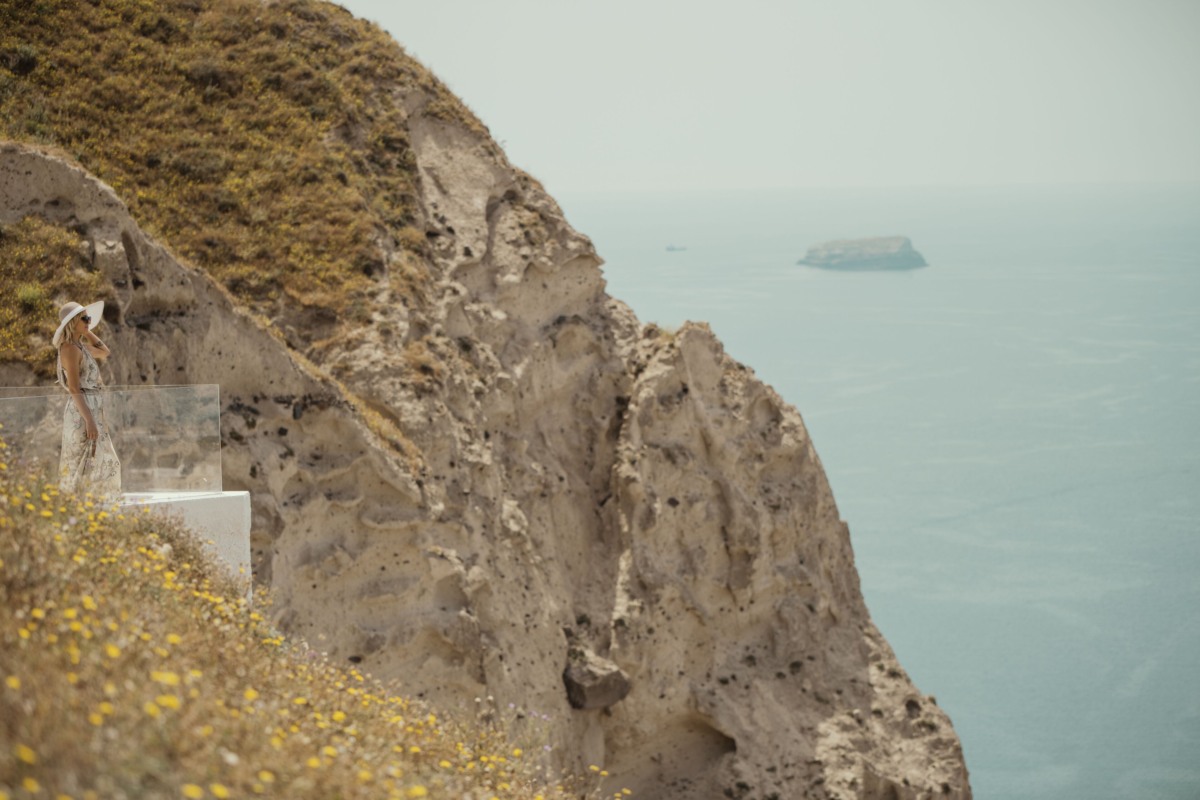 A cliffside with a person standing on a transparent platform overlooking the sea.