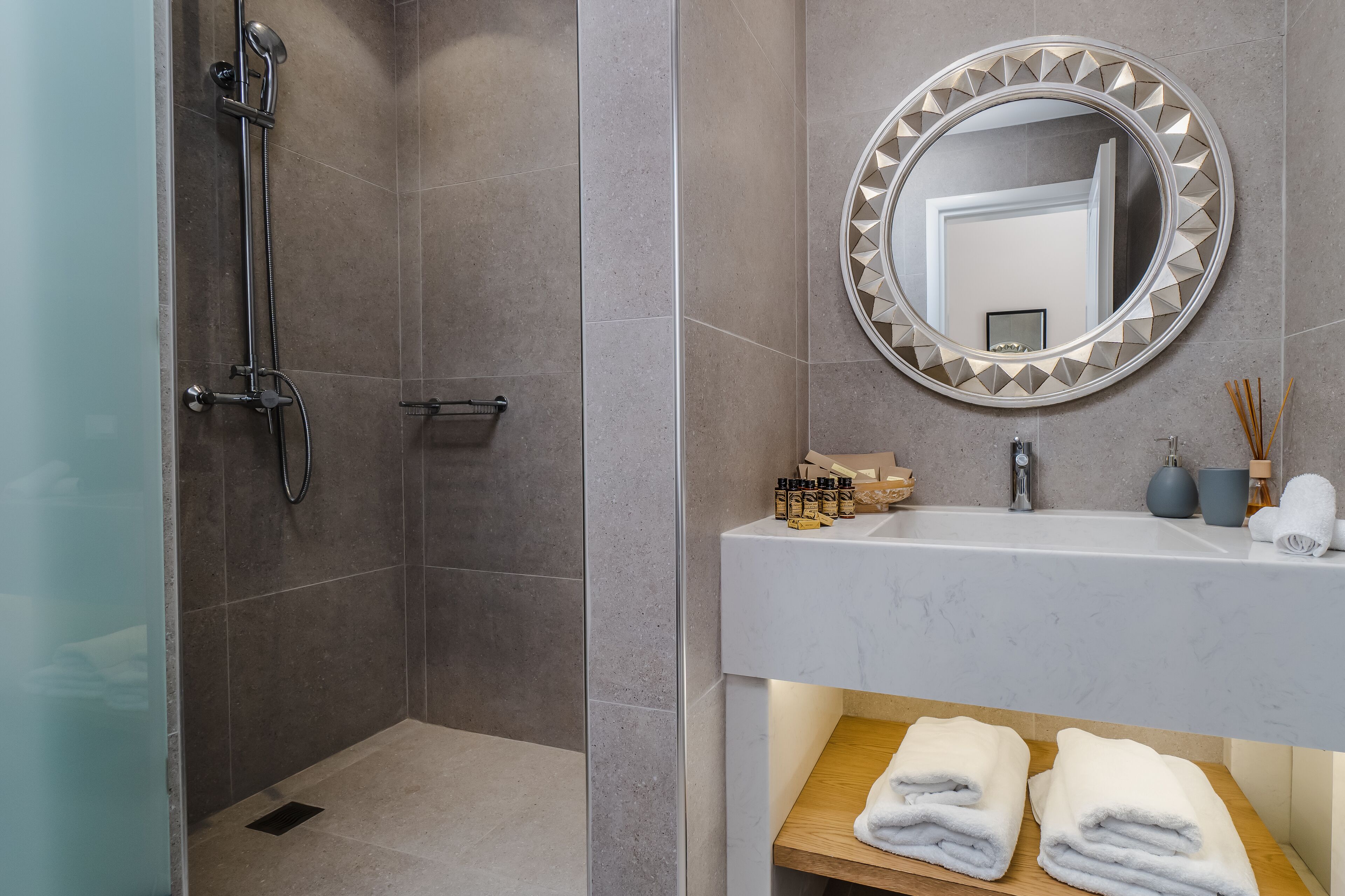 Ein modernes Badezimmer mit Dusche, Waschbecken und Pflegeprodukten sowie einem Spiegel mit dekorativem Rahmen.