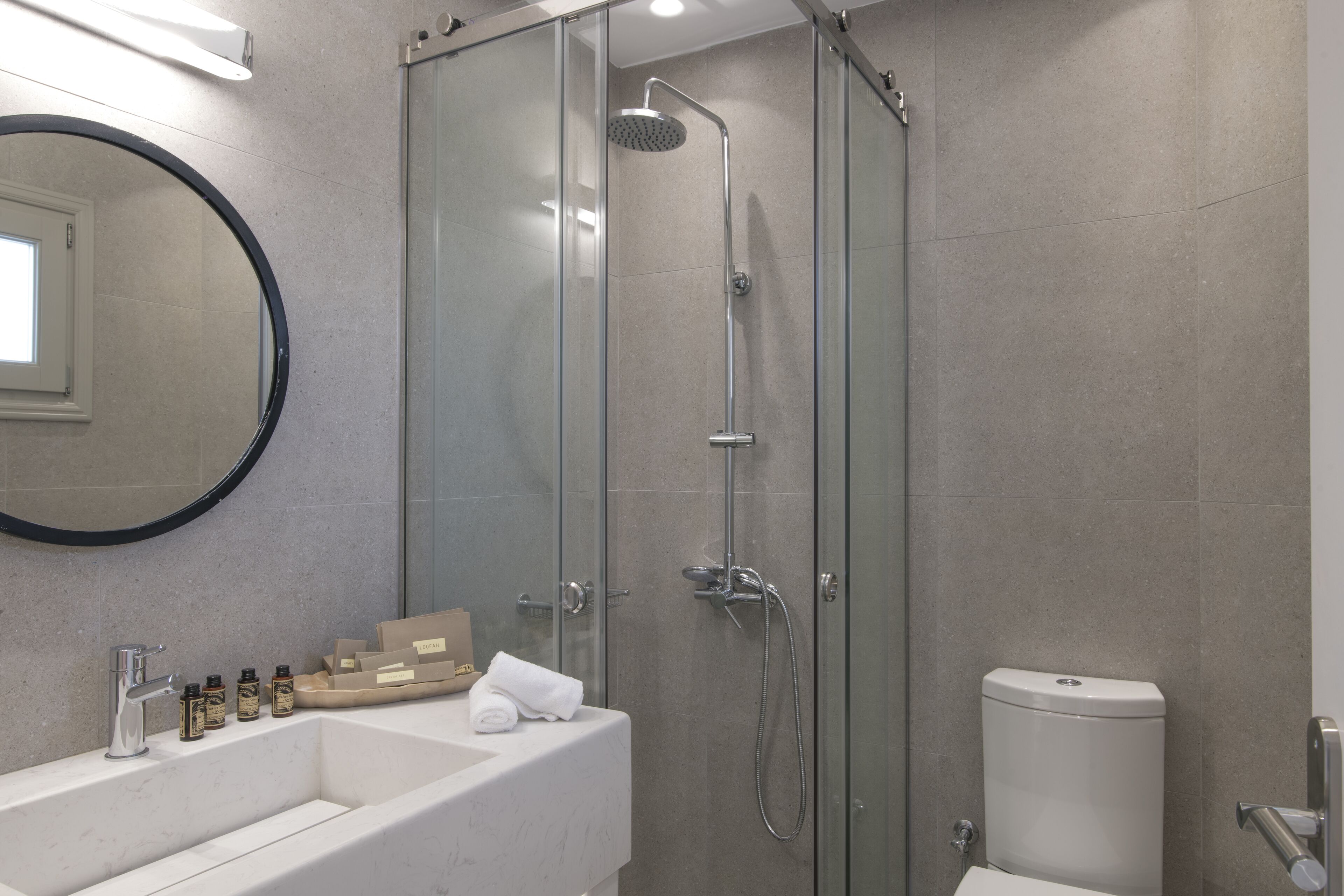 A modern bathroom with a glass-enclosed shower, a white sink with toiletries, and a toilet.