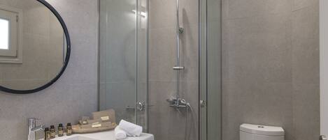 Un baño moderno con cabina de ducha de vidrio, un lavabo blanco con artículos de aseo y un inodoro.