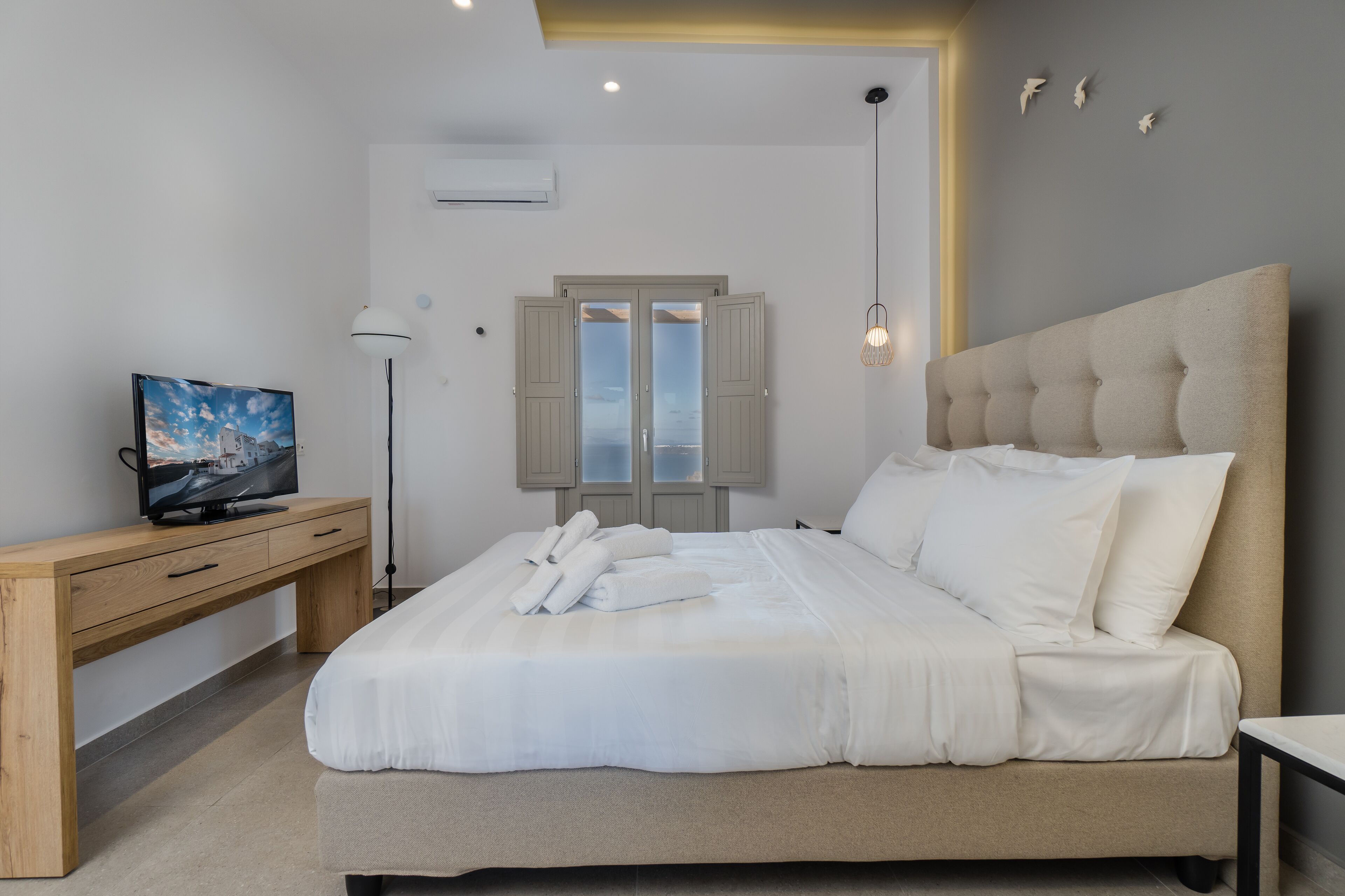A bedroom with a bed, a desk, a television, and a window with shutters.