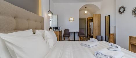 A hotel room with a large bed, a desk with two chairs, a small table, and a mirror.