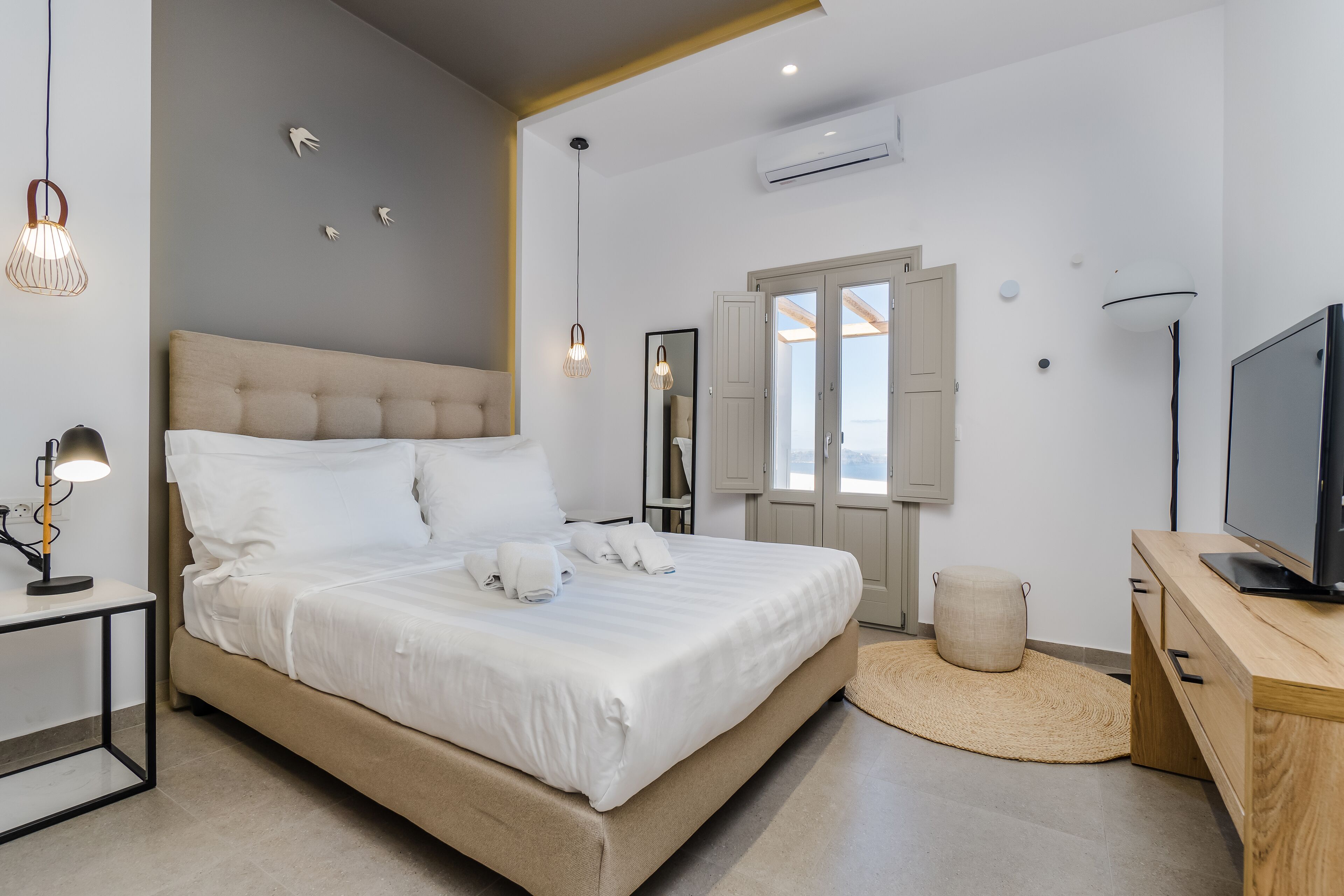 Ein modernes Schlafzimmer mit einem großen Bett, Nachttischen, einem Fernseher und Blick ins Freie.