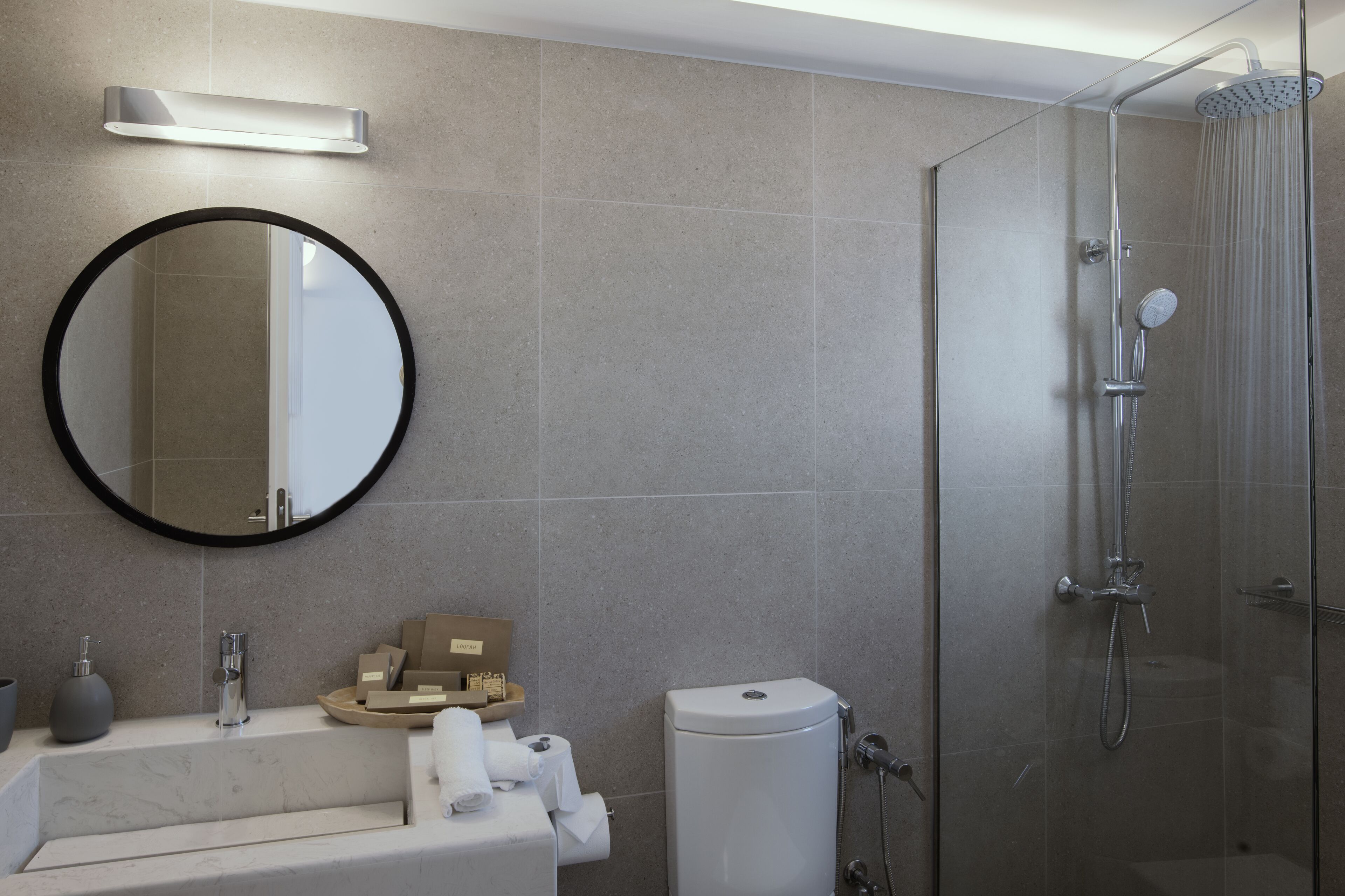A modern bathroom with a round mirror, a bathtub, a toilet, and a glass-enclosed shower.