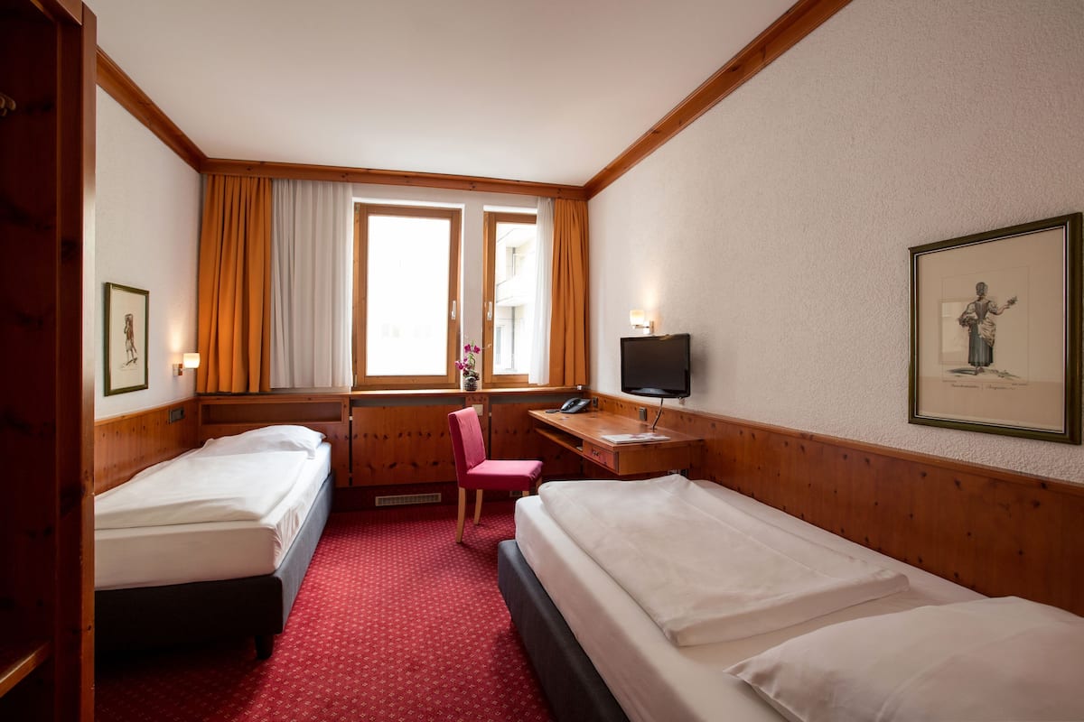 A hotel room with two beds, a desk, a chair, a TV, and a window with curtains.