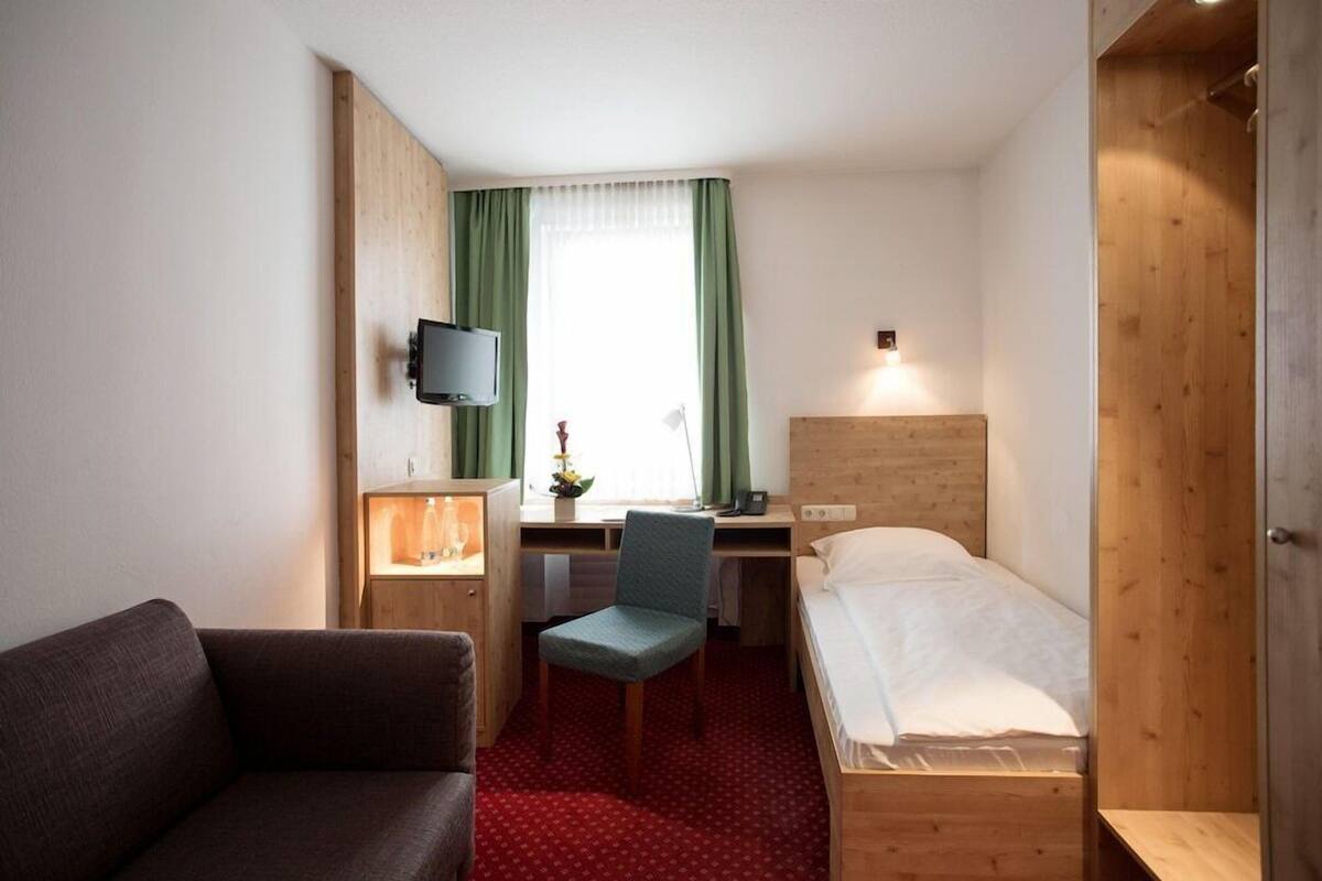 A compact hotel room with a single bed, a desk with a chair, a television mounted on the wall, and a wardrobe.