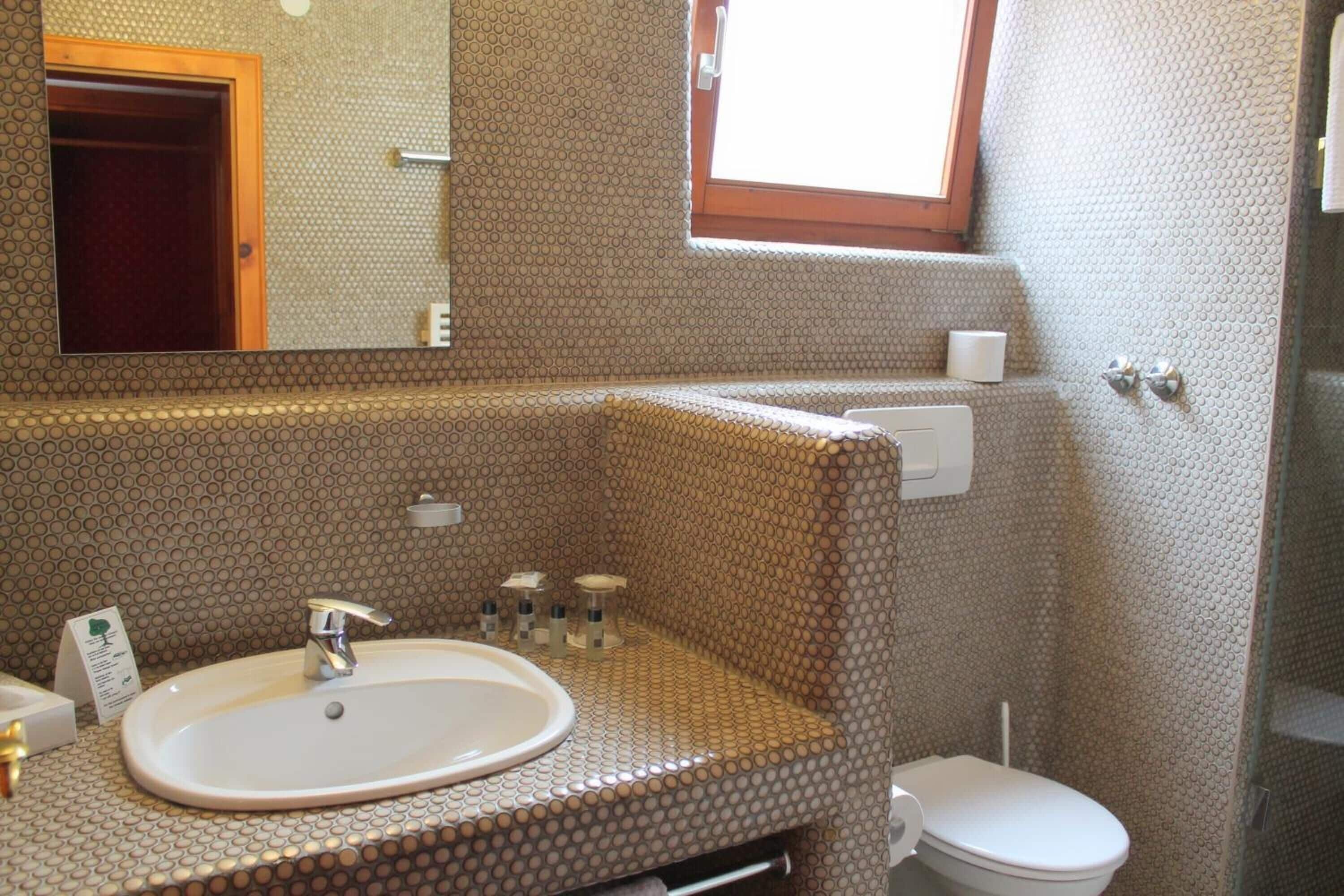 Un baño con lavamanos, espejo, inodoro y ventana.
