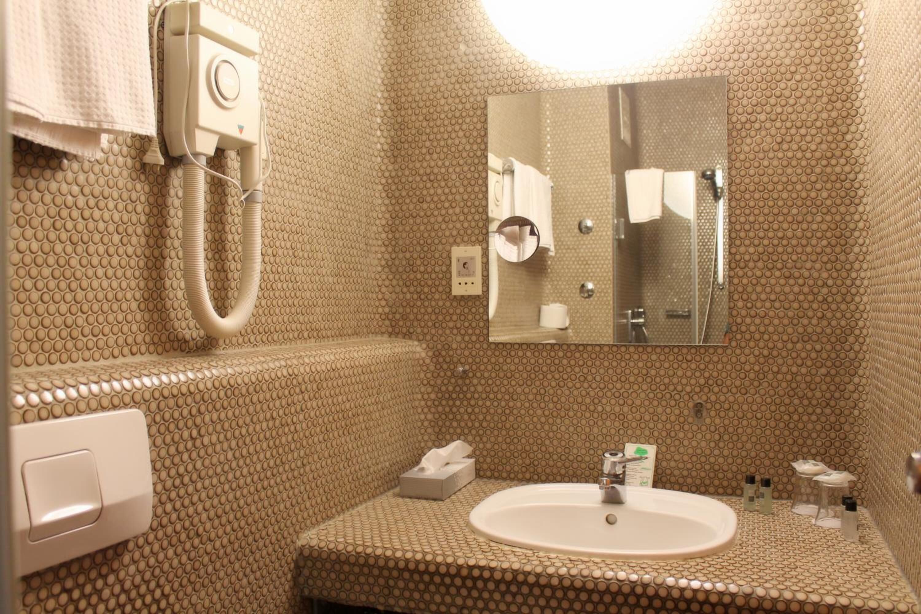 A bathroom with a textured wall, a sink, a mirror, a towel rack, and a handheld showerhead.
