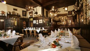 Un restaurante con varias mesas dispuestas para comensales, con candelabros y cuadros en las paredes.