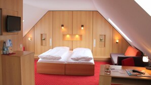 Una habitación de hotel con una cama nido de madera, un escritorio con lámpara, un televisor montado en la pared y una alfombra roja.