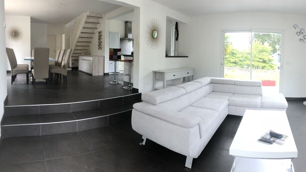 A modern living room with a sectional sofa, a dining area with chairs, a kitchen area, and a staircase leading to an upper level. - House 8 persons Tréboul (Douarnenez)