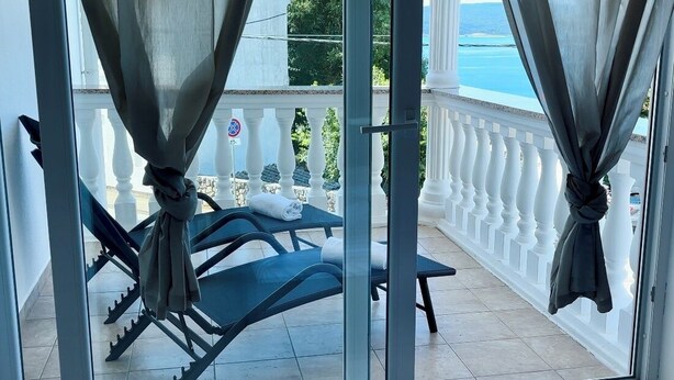 Un balcone con ringhiera bianca, un tavolo e due sedie.