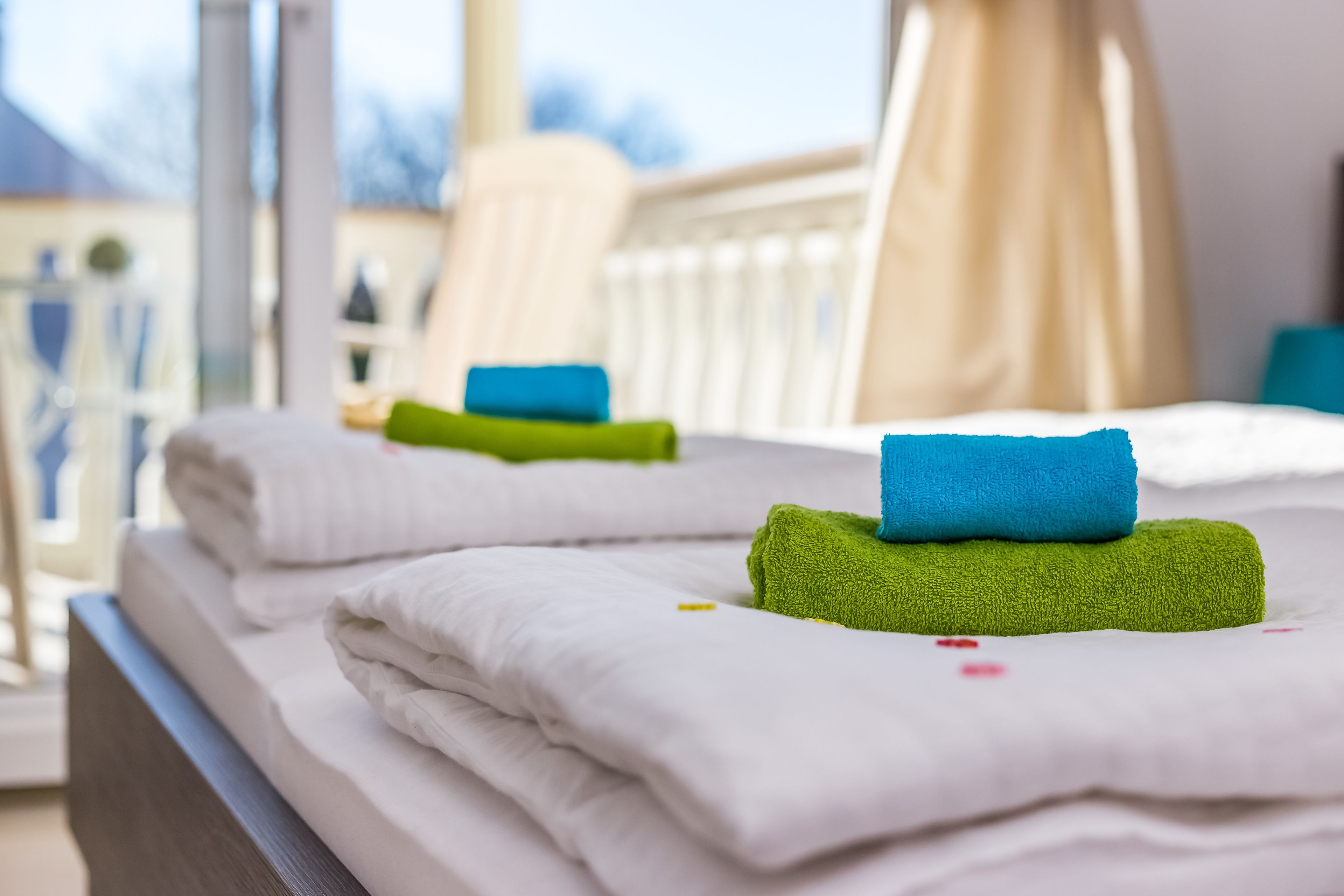 Ett hotellrum med prydligt hopvikta vita handdukar och en grön handduk på sängen.