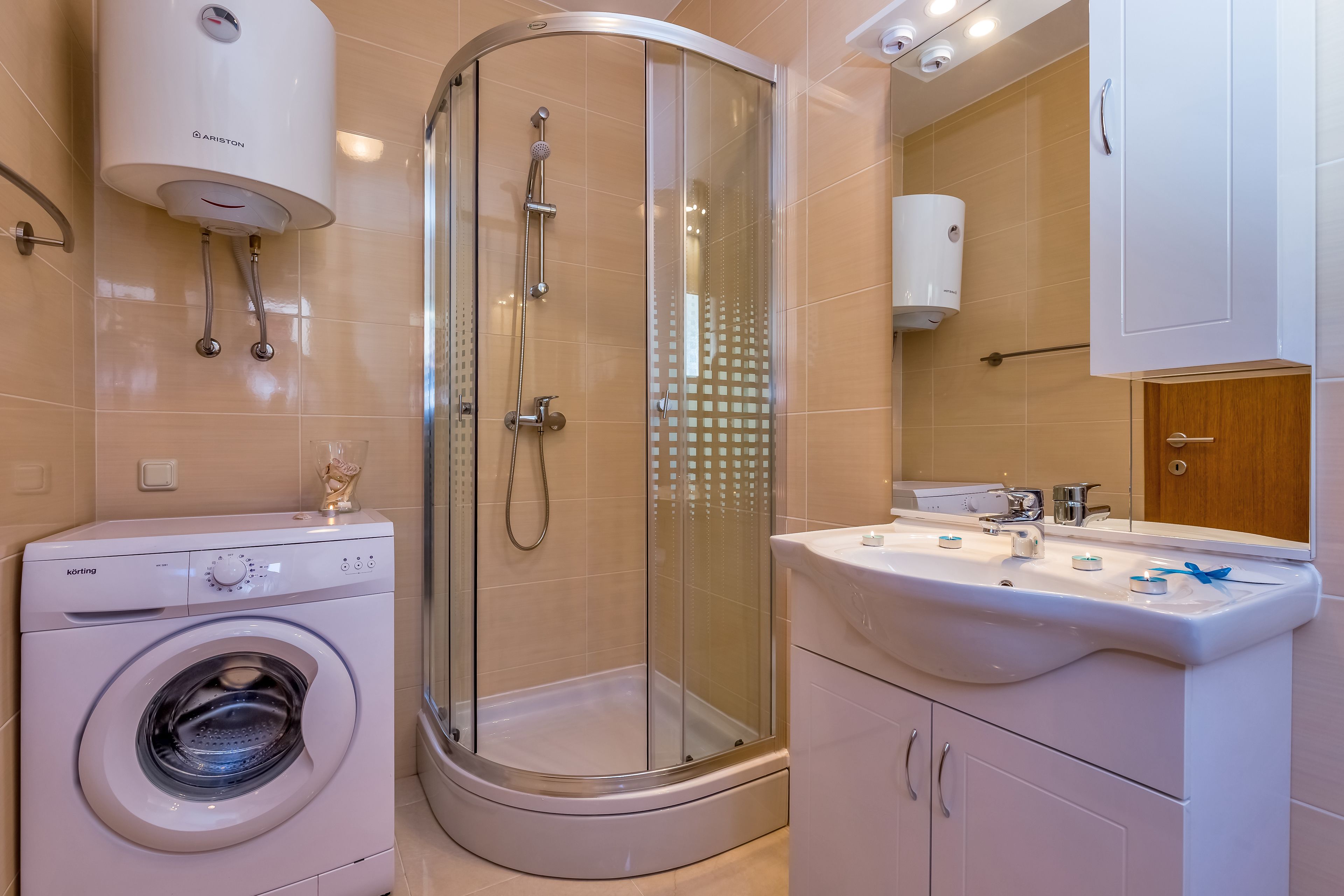 A modern bathroom with a glass-enclosed shower, a washing machine, and a sink with a mirror.