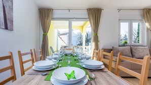 Un'area pranzo con un tavolo apparecchiato per sei persone, sedie, un divano e vista panoramica attraverso una porta in vetro.