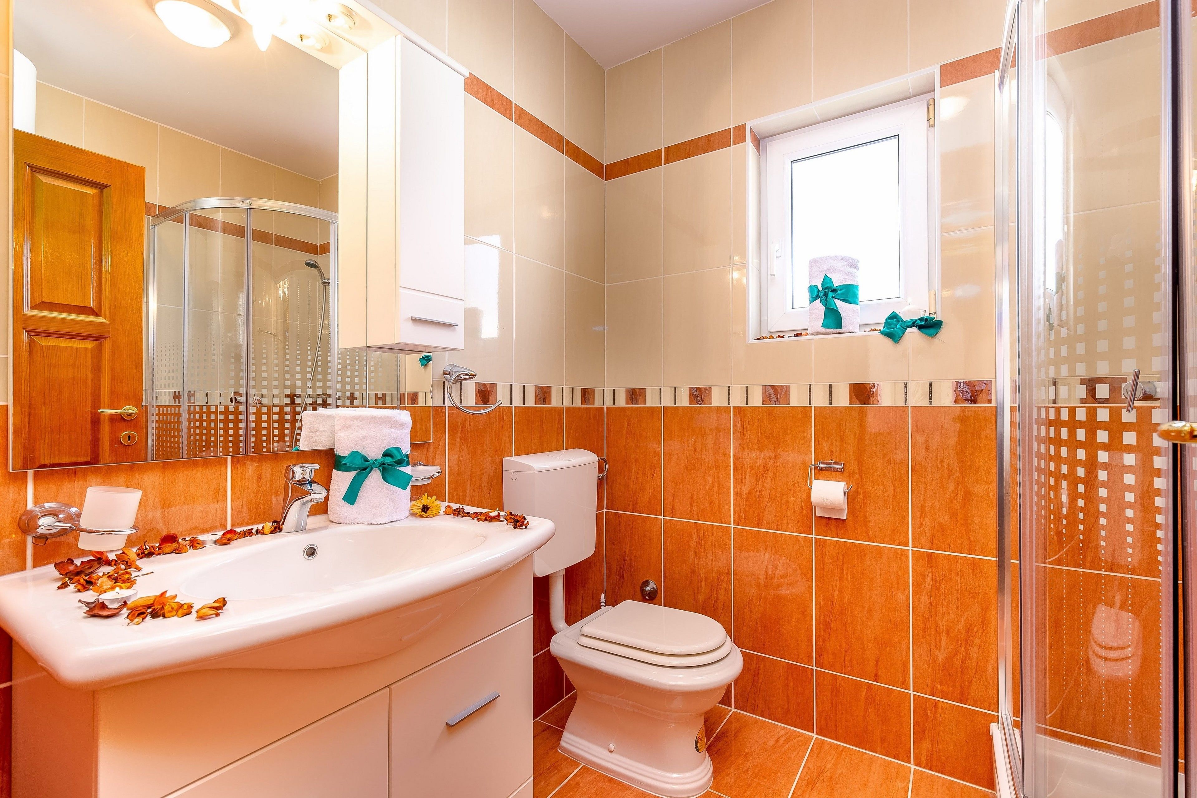 A bathroom with a shower, toilet, sink, and a window with a towel and bow.