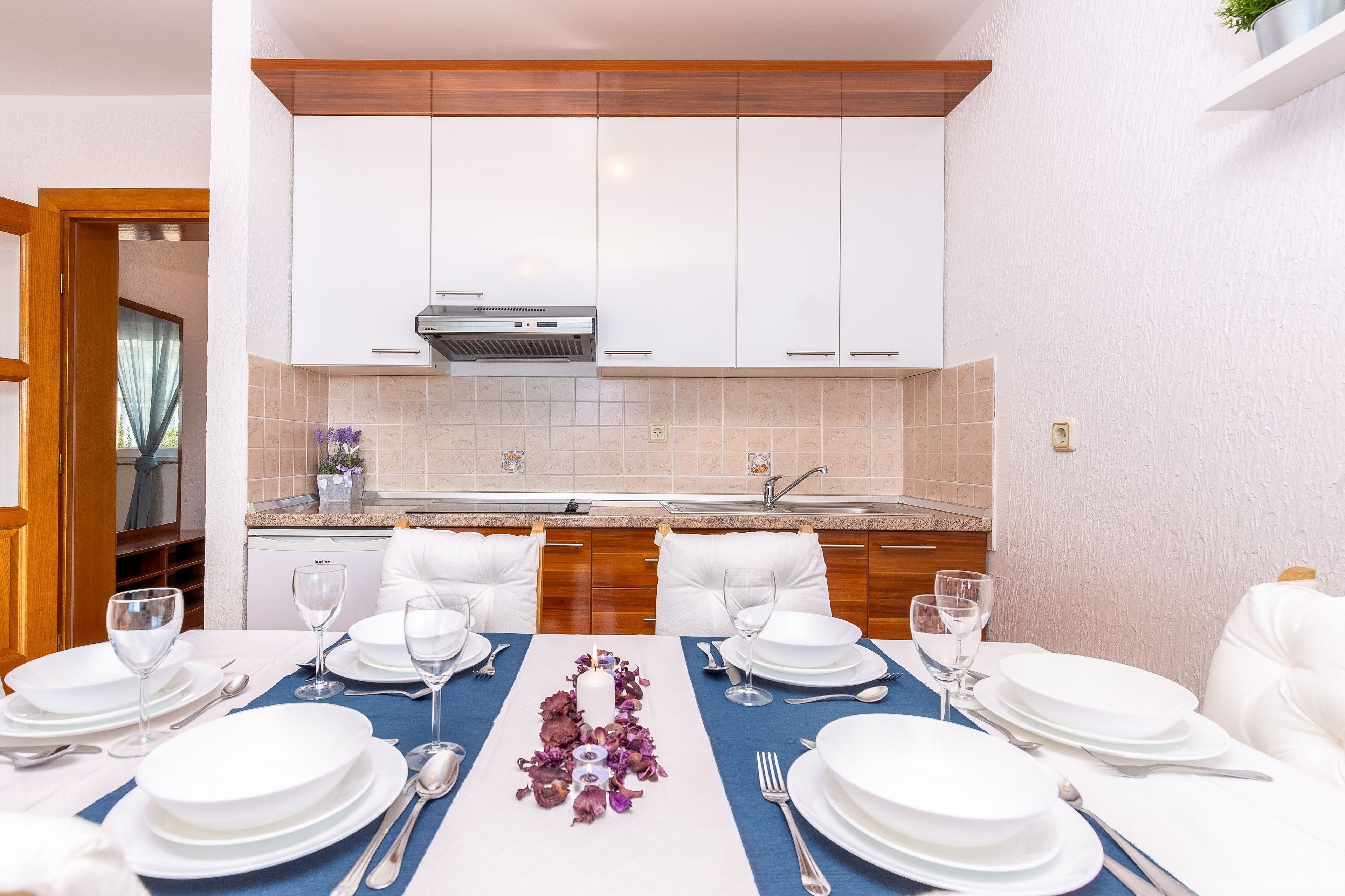 A modern kitchen with white cabinets, a stainless steel range hood, and a built-in dishwasher.