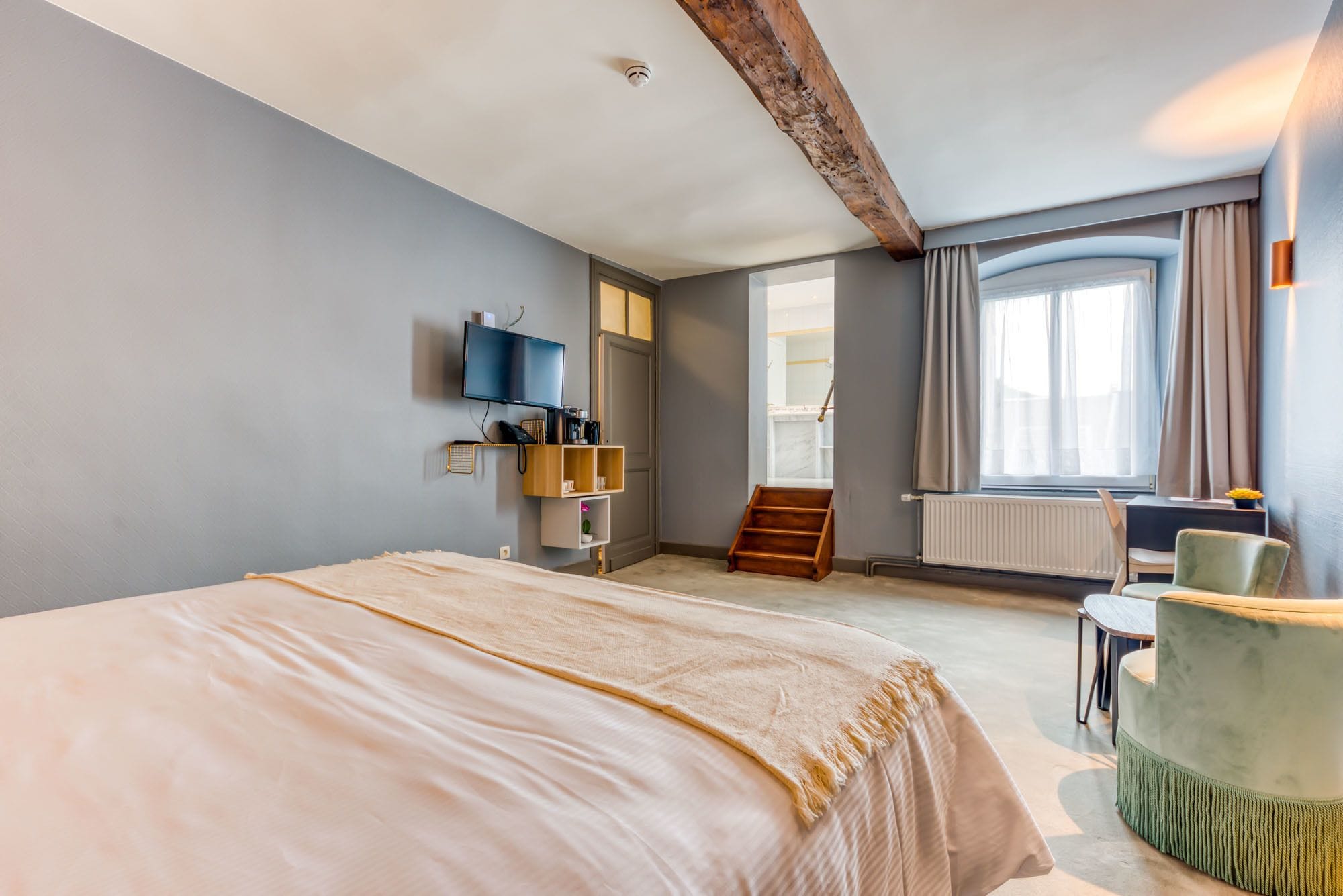 A hotel room with a large bed, a desk with a chair, a television, and a window with curtains.