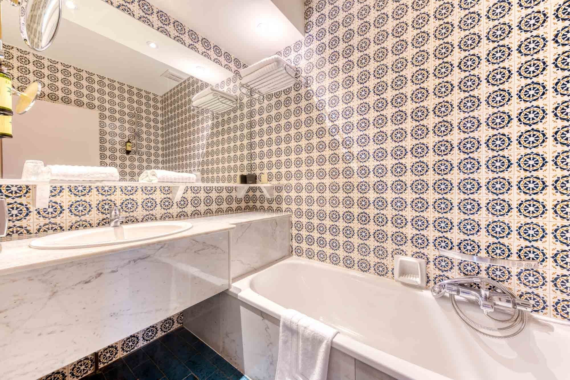 A bathroom with a white sink, a bathtub, and a mirror. The walls are tiled with a blue and white pattern.