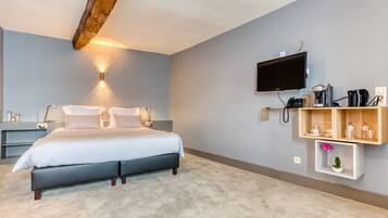A modern hotel room with a large bed, a mounted TV, a coffee machine, and a shelf with toiletries.