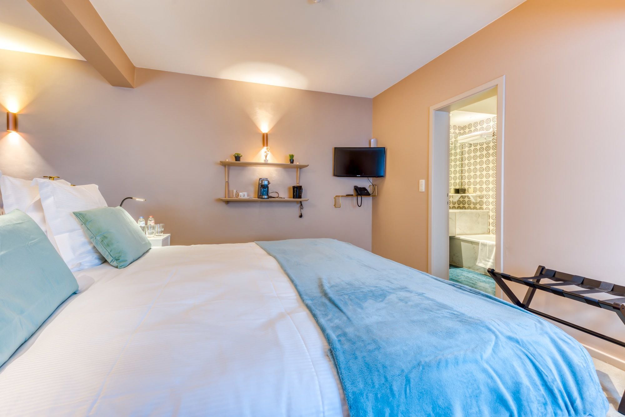 A hotel room with a bed, bedside tables, a TV, and a bathroom visible through an open door.