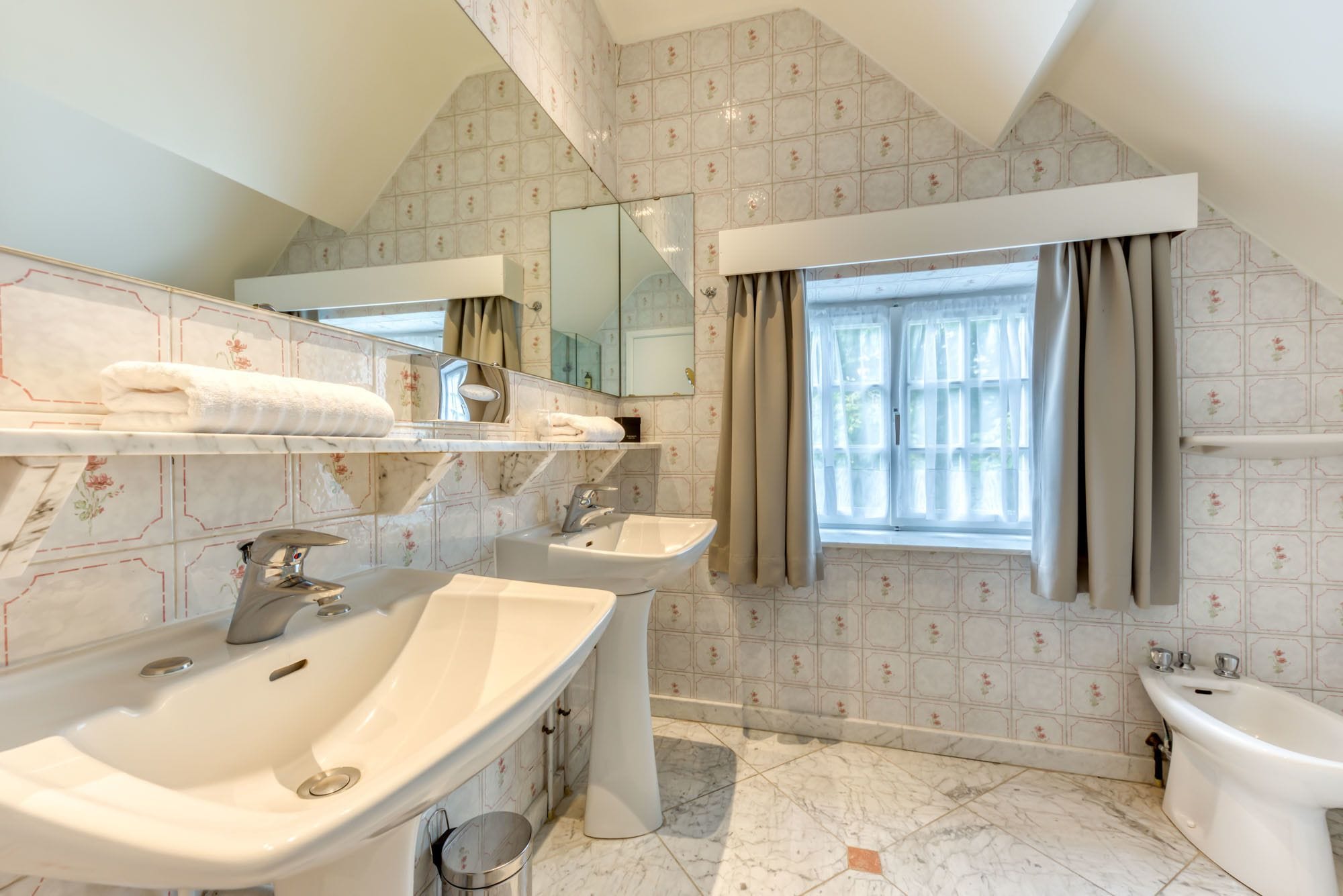 A bathroom with a large mirror, two sinks, a bathtub, and a window with curtains.
