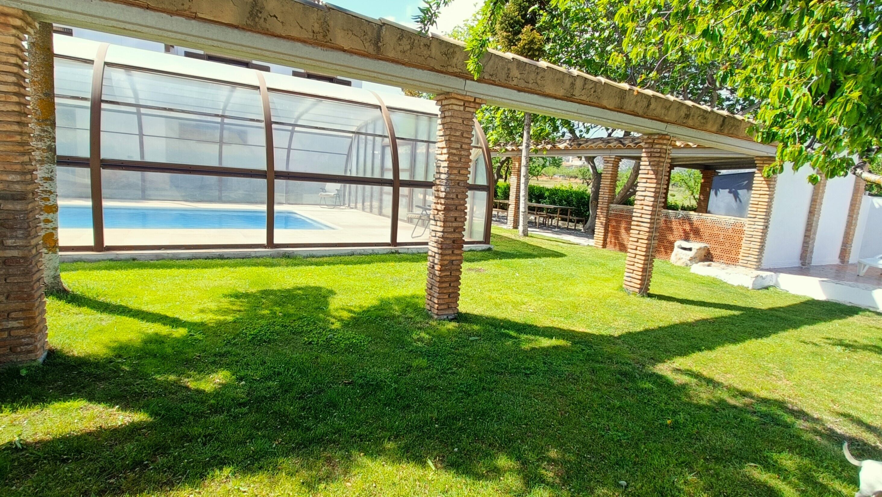 Ein moderner Außenbereich mit Schwimmbecken, überdachter Terrasse und Ziegelstützen.