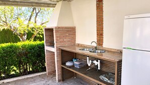 Cocina exterior con horno de ladrillo, dos fregaderos y un refrigerador.