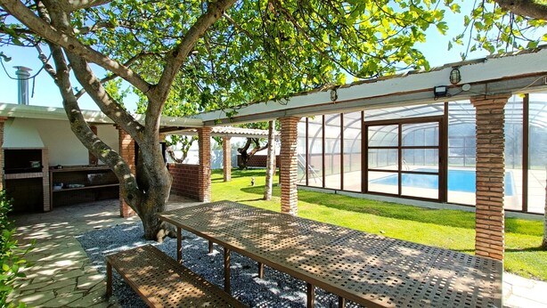 Un patio techado con piscina, una parrilla y una estructura de pérgola.