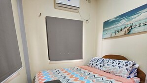Une chambre à coucher avec un lit, une fenêtre avec un store, un appareil de climatisation et un tableau au mur.