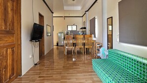 Une pièce spacieuse avec une table à manger en bois, des chaises, un canapé à motifs verts et un ventilateur de plafond.
